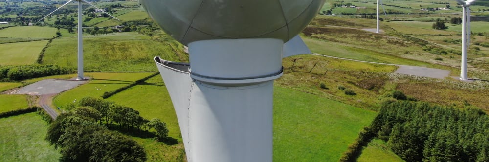 The hub of a wind turbine on a blue sky day with green fields in the background